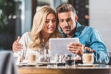 happy affectionate couple using digital tablet in cafe