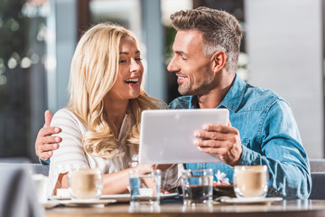 happy couple using tablet at table in cafe