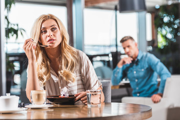 pensive beautiful blonde woman eating dessert with flower in cafe