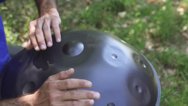 Musician hands playing handpan drum in nature scene.