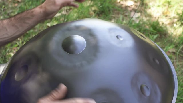 Musician hands playing handpan drum in nature scene.