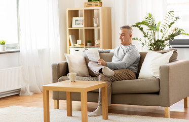 leisure, information, people and mass media concept - man reading newspaper at home