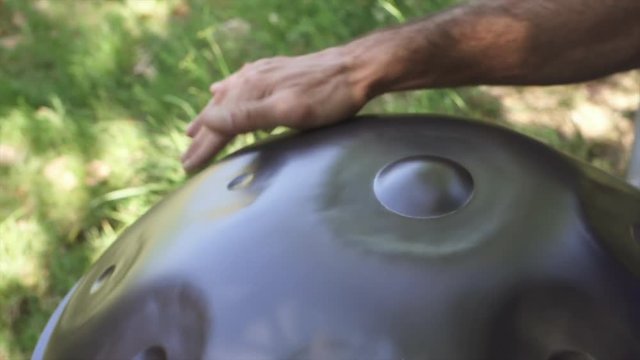 Musician hands playing handpan drum in nature scene.