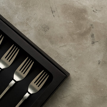 Top view of silver collection of knives forks spoons tablespoons and teaspoons in a black box on a gray concrete background