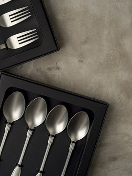 Top view of silver collection of knives forks spoons tablespoons and teaspoons in a black box on a gray concrete background