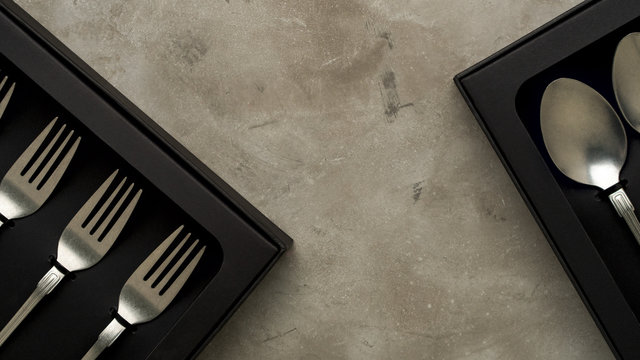 Top view of silver collection of knives forks spoons tablespoons and teaspoons in a black box on a gray concrete background