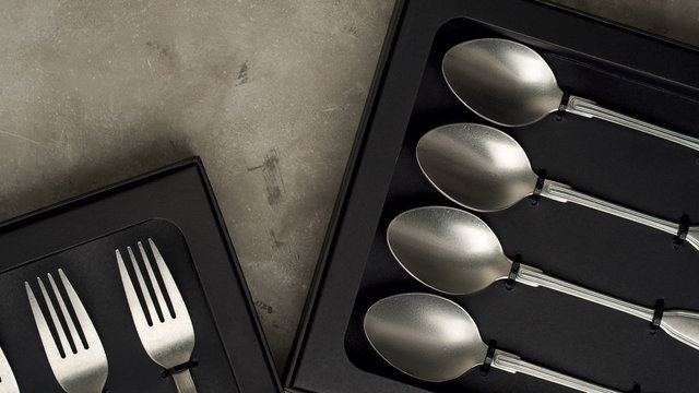 Top view of silver collection of knives forks spoons tablespoons and teaspoons in a black box on a gray concrete background