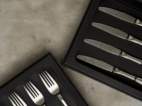 Top view of silver collection of knives forks spoons tablespoons and teaspoons in a black box on a gray concrete background
