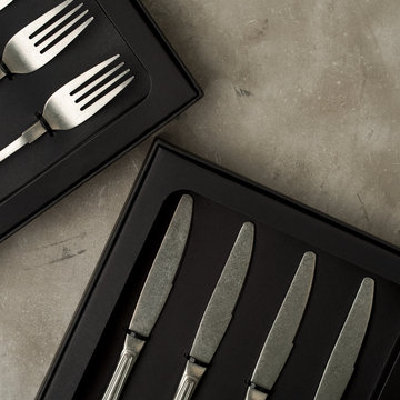 Top view of silver collection of knives forks spoons tablespoons and teaspoons in a black box on a gray concrete background