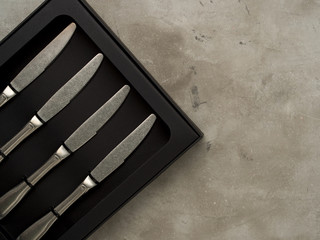 Top view of silver collection of knives in a black box on a gray concrete background