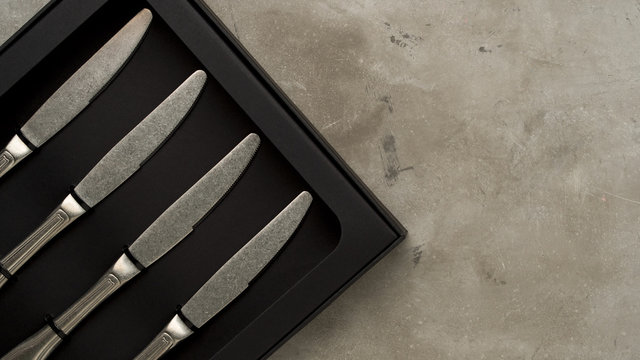Top view of silver collection of knives in a black box on a gray concrete background