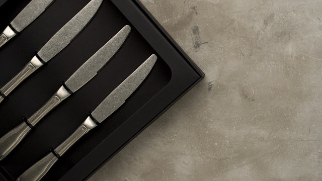 Top view of silver collection of knives in a black box on a gray concrete background