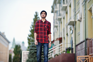 Young indian student man at red checkered shirt and jeans walking at city.