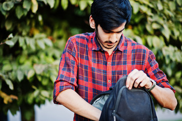 Obraz premium Young indian student man at red checkered shirt and jeans with backpack posed at street.