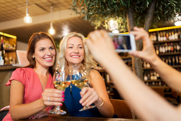 people, technology and lifestyle concept - woman photographing friends drinking wine by smartphone at bar or restaurant