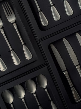 Top view of silver collection of knives forks spoons tablespoons and teaspoons in a black box on a gray concrete background
