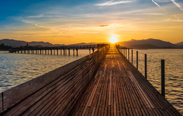 Dramatic sunrise during the Fall Equinox over the historical holzsteg pedestrian bridge crossinhg the Upper Zurich Lake (Obersee), part of the old Way of Saint James, Switzerland