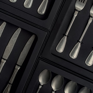 Top view of silver collection of knives forks spoons tablespoons and teaspoons in a black box on a gray concrete background