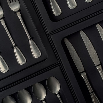 Top view of silver collection of knives forks spoons tablespoons and teaspoons in a black box on a gray concrete background