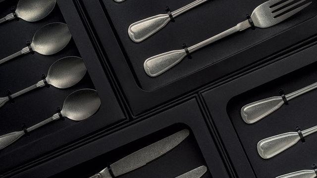 Top view of silver collection of knives forks spoons tablespoons and teaspoons in a black box on a gray concrete background