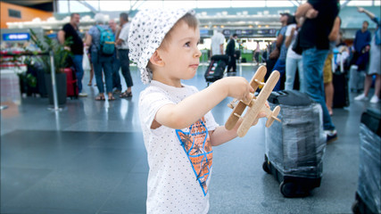 Portrait of 2 years old toddler boy playing with toy airplane in airport