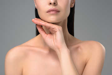 cropped shot of young naked brunette woman touching chin isolated on grey