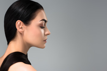 profile of beautiful young brunette woman looking away isolated on grey