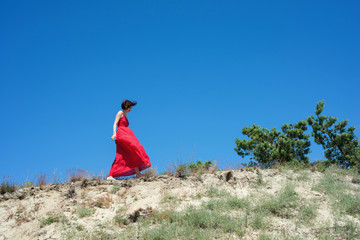 
Young brunette woman in a red dress walking on a mountainside
