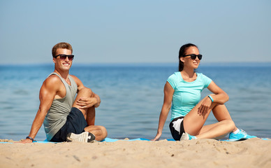 Fototapeta premium fitness, sport and lifestyle concept - smiling couple stretching legs on beach before training
