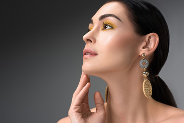 young brunette woman with beautiful earrings looking up isolated on grey