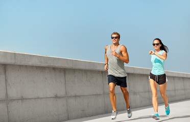 fitness, sport and lifestyle concept - happy couple in sports clothes and sunglasses running...