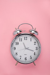 Top view of a classic analog alarm clock on pink background with copy space