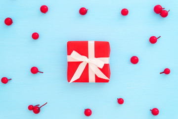 Christmas composition.  Red gift box and red berries on blue background. Creative flat lay, top view design