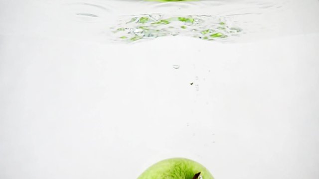 The green apple falls into the water. Isolated apple on white background in slow motion.