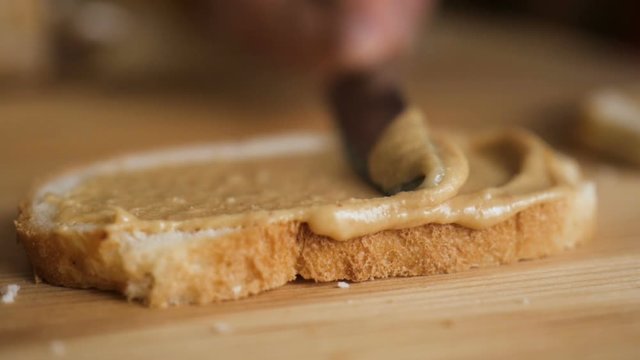 Delicious and hearty breakfast nut cream on a crisp bread. Man makes a peanut butter sandwich.. Closeup of male hands spreading butter on bread in kitchen,  slow motion.