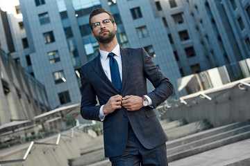 A young businessman fastens a suit jacket. He has on his hands an expensive watch.