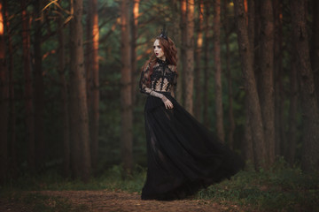 Fototapeta na wymiar A beautiful gothic princess with pale skin and very long red hair in a black crown and a black long dress in a misty fairy forest. The costume of the dark queen.