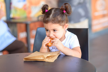 Kid devours croissant. Cute Little girl having breakfast in the cafe on the city street. The child is eating a croissant. Breakfast black table at restaurant, eco paper bag.