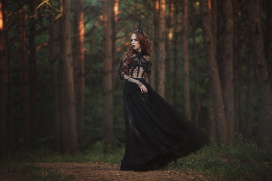 A Beautiful Gothic Princess With Pale Skin And Very Long Red Hair In A Black Crown And A Black Long Dress In A Misty Fairy Forest. The Costume Of The Dark Queen.