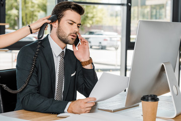 businessman talking by smartphone and secretary giving him handset of stationary telephone