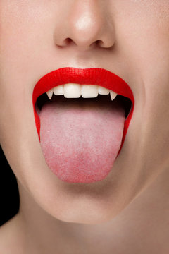 Macro photo of sexy female lips with red scarlet lipstick. Woman shows her tongue and snow-white teeth with fangs like a vampire. Dentistry, cosmetology, halloween