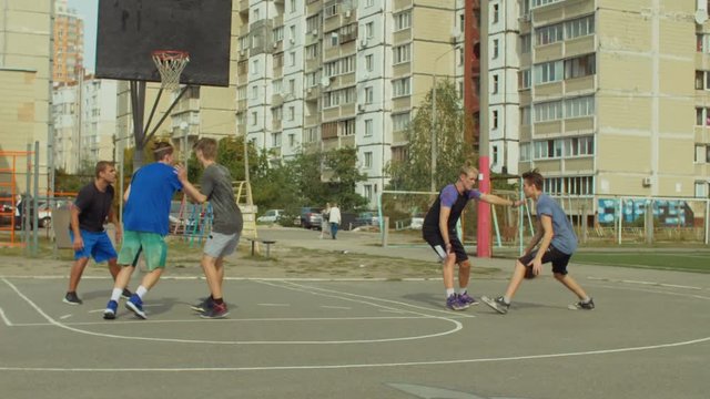 Teenage sporty basketball player dribbling and passing the ball to his teammate while playing streetball on court. Streetball player scoring points in the paint with layup shot during basketball game.