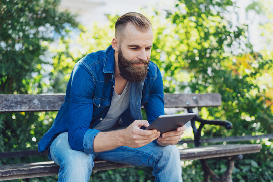 Young bearded man in jeans using a tablet pc