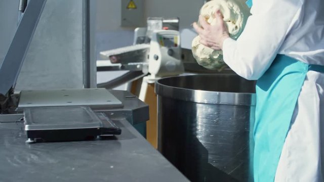 Male food production worker in protective clothing taking fresh dough from container and putting it on table at factory