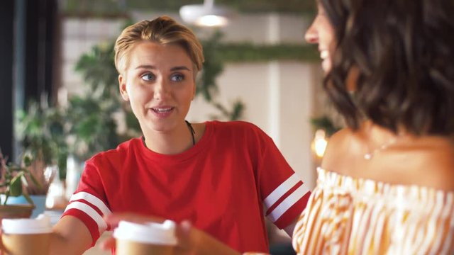 people, communication and friendship concept - female friends drinking coffee and talking at cafe
