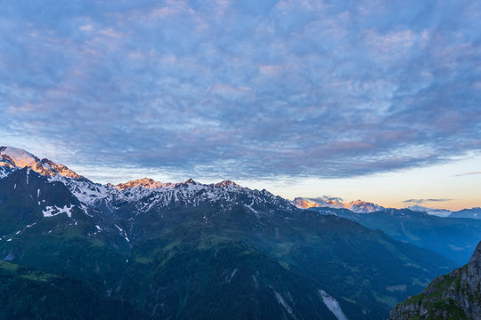 Scenic view of beautiful Swiss Alps mountains. Dramatic early morning scene in high mountains with first light. Blue hour sunrise with pink and blue tones, Switzerland.