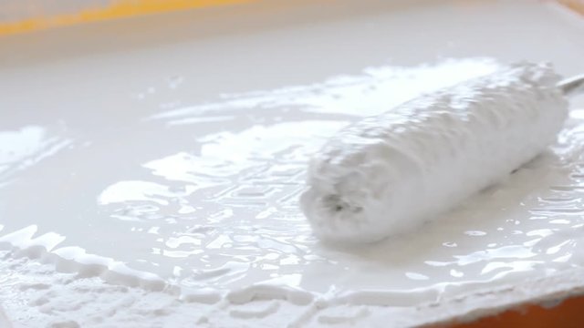Covering of roller on handle with white paint 4k footage.