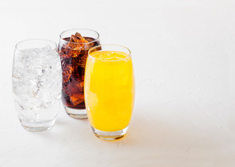 Glasses of soda drink with ice cubes and bubbles on stone kitchen table background. Cola and orange lemonade soda