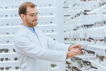 smiling oculist taking eyesight from shelves in ophthalmic shop