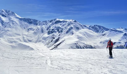 Afwasbaar fotobehang skiër op een helling in alpine besneeuwde berg onder blauwe hemel © coco